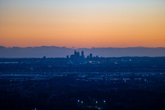 Aerial view of the Perth skyline silhouetted against a vibrant sunset sky with city lights beginning to glow across the urban landscape in Western Australia, Australia.