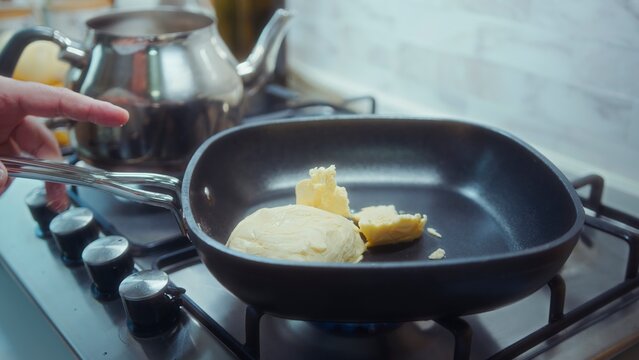Cooking butter melting in a black frying pan on a gas stove in a modern kitchen with stainless kettle in background