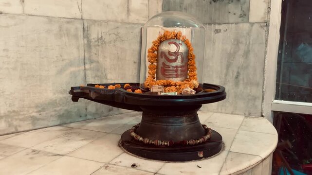 Shivalinga decorated with fresh flower garlands and placed on a traditional yoni pedestal inside a Hindu temple. The revered symbol of Lord Shiva represents cosmic creation, divine energy, 