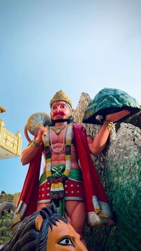 Majestic statue of Lord Hanuman carrying the Sanjeevani mountain and holding a gada (mace), beautifully decorated with flower garlands at a Hindu temple.