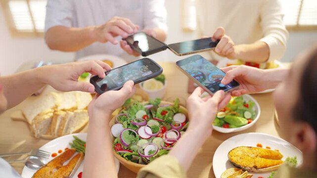 Happy Multi-generation Asian family using smartphone taking photos of healthy homemade meal at dining table, capturing food images for social media content, family bonding and digital lifestyle at hom