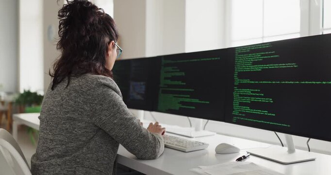Businesswoman developer programmer coding software on computer. Focused engineer reviews code on multiple monitors at a modern workstation. Concept highlights technology productivity and focus.