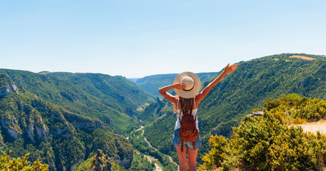 Happy and freedom female hiker with backpack looking at canyon landscape with raised arm