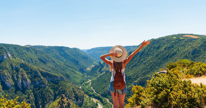 Happy and freedom female hiker with backpack looking at canyon landscape with raised arm