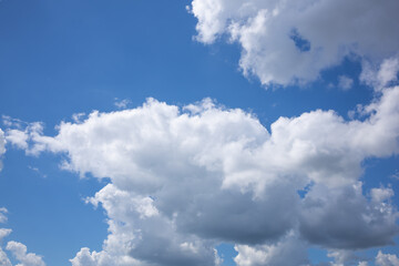 Fototapeta premium Bright daytime sky with textured white clouds. Beautiful dramatic blue sky with large white cumulus clouds before summer rain. Natural cloudscape with dynamic formations