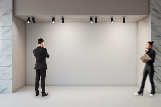 Businesspeople observing an empty gallery wall under spotlights in a modern museum interior room with marble accents and soft lighting concept scene.
