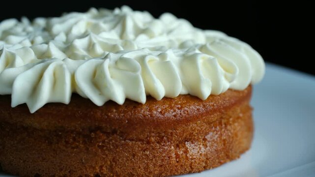 Delicious homemade cake decorated with creamy white frosting, rotating on white plate, showing off its perfect sweet and fluffy texture in close up shot. Delicious frosted cake rotating on dish