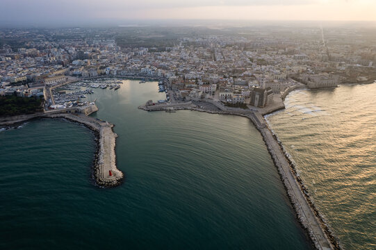 Aerial view of the historic harbor and Trani Cathedral with stone breakwaters and calm sea at sunset, Trani, Apulia, Italy.