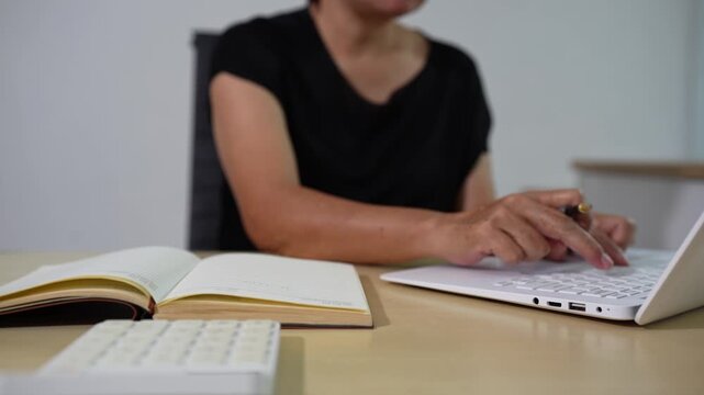 Employee, taking notes sitting at desk using smartphone and laptop searching for information at work.