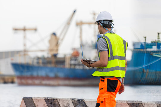 Logistics engineer using laptop to monitor cargo operations at shipping port, Worker inspecting freight transport at terminal, Marine logistics specialist managing shipping cargo activities at harbor