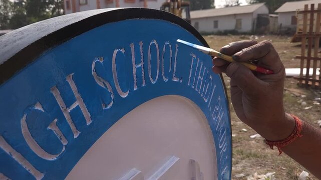 Authentic footage of an Indian stone sculpture artist hand-painting a Platinum Jubilee commemorative school logo sculpture in Odisha, India. The video showcases traditional craftsmanship