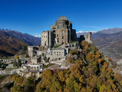 Aerial view of the historic Sacra di San Michele abbey perched on a rocky mountain peak surrounded by autumn forests in Sant'Ambrogio di Torino, Piemonte, Italy.