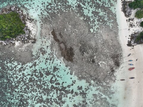 Aerial view of Koh Lipe Pier with long-tail boats on the beach, adjacent to a shallow coral reef and turquoise water in Tambon Ko Tarutao, Chang Wat Satun, Thailand.