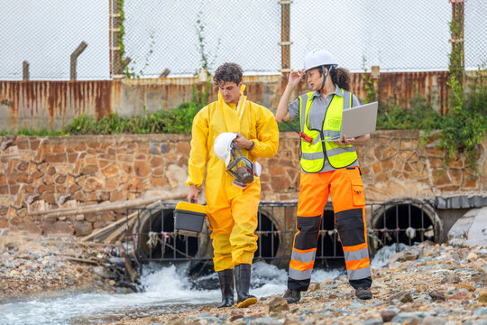 Professional team with lab equipment and laptop in protective gear monitoring pollution at drainage system, Environmental specialists conducting water quality inspection at an industrial site