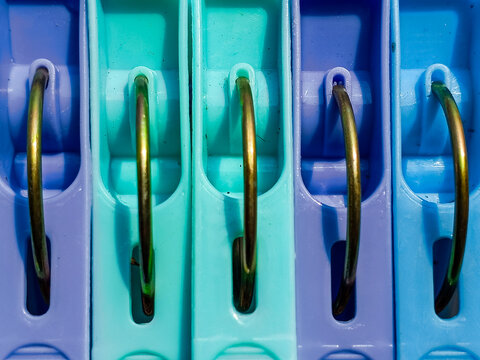 Macro close-up of colorful plastic clothespins with metal springs aligned in a row under bright sunlight. Perfect vibrant background for laundry day, household chores, and home organization concepts.