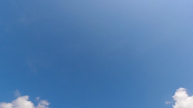Clear blue sky in the late afternoon with a fluffy white cloud in the corner. Perfect minimalist background with ample negative space for text and graphics.