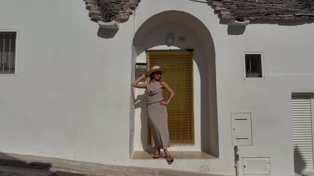 Stylish Female Traveler Posing in Traditional Arched Doorway of Whitewashed Trullo House in Alberobello, Puglia, Italy