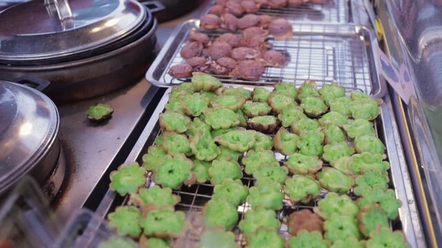 Thai Street Food Desserts Fried Pandan Pancake (Khanom Fak Bua) & Coconut Pudding Pancake (Khanom Krok). Vendor Sells Fresh Cooked Sweet Snacks at Open Street Food Night Market in Bangkok Thailand.
