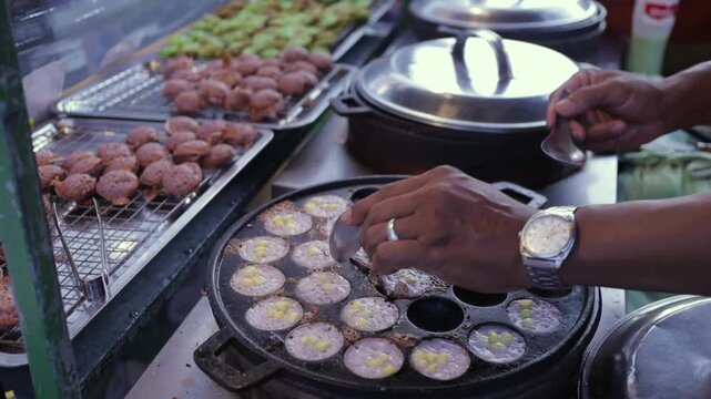 Open Market Vendor Cooking Thai Dessert Coconut Pancakes (Khanom Krok). Asian Street Food Night Market in Bangkok Thailand