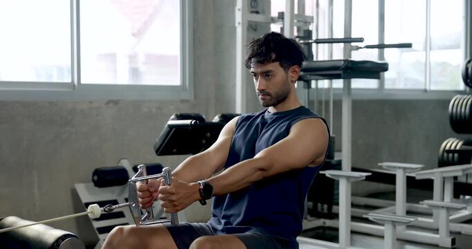 Young Asian man performs seated cable row in modern gym, pulling grip handle with controlled movement, solo upper body strength training, back muscle workout, wellness, healthy lifestyle routine.