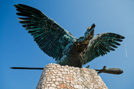 Bronze Turul Statue with Condrail and Airplane in the Blue Sky. Historic Hungarian mythological bird monument with modern aviation trail contrast.