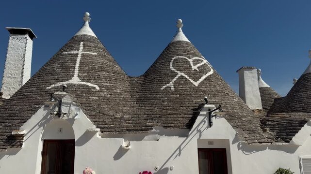 Traditional Trulli Conical Stone Roofs with Painted Symbols Under Blue Sky in Alberobello, Puglia, Italy