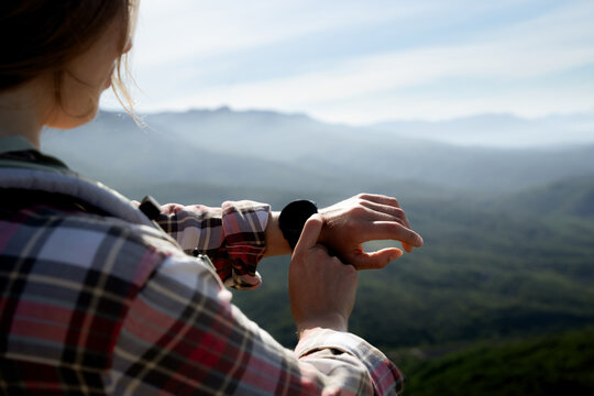 A woman is using a smartwatch while on a hiking trip, with blurred mountain scenery in the background. It's useful outdoor technology for an active lifestyle.
