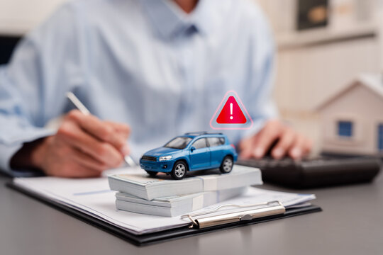 Auto loan debt and car finance risk concept. Toy car on money cash with red warning alert icon and man calculation.