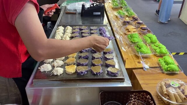 Thai Dessert, Authentic Coconut Pancake Macaroon (Khanom Babin). Vendor Woman Cooking and Turning Cakes on Hot Pan Skillet at Asian Bangkok Thailand Street Food Open Night Market