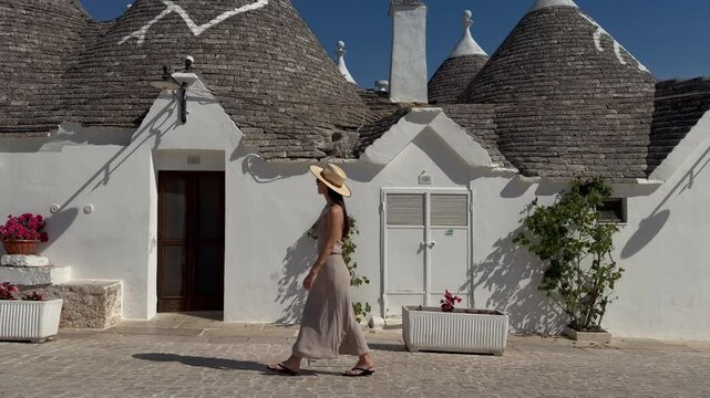 Female Traveler Walking Past Traditional Whitewashed Trulli Houses and Conical Roofs in Alberobello, Puglia, Italy