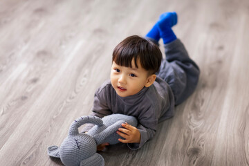 Naklejka premium A cute Asian boy wearing a gray sweater plays indoors.