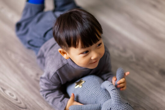 A cute Asian boy wearing a gray sweater plays indoors.