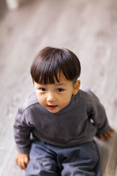 A cute Asian boy wearing a gray sweater plays indoors.