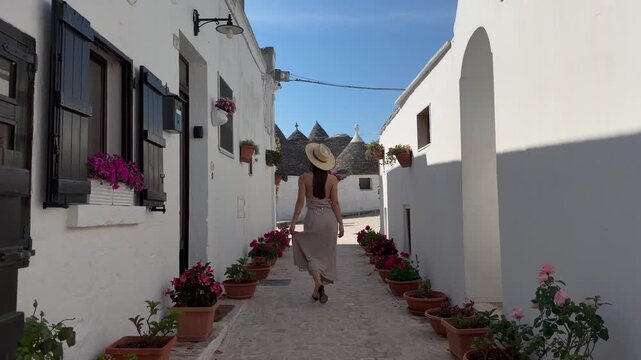 Woman Walking Along Picturesque Flower-Lined Trulli Street in Alberobello, Puglia, Southern Italy