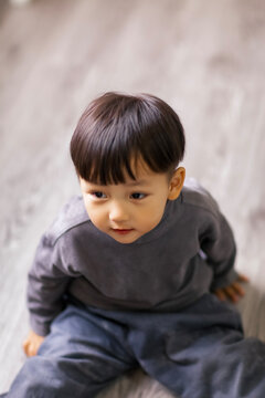 A cute Asian boy wearing a gray sweater plays indoors.
