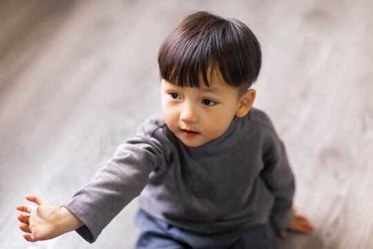 A cute Asian boy wearing a gray sweater plays indoors.