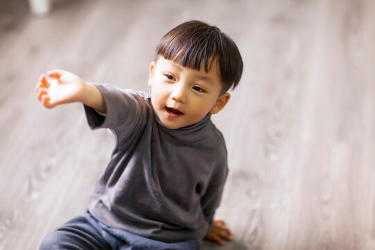 A cute Asian boy wearing a gray sweater plays indoors.