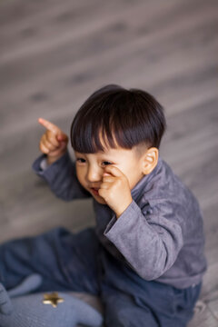 A cute Asian boy wearing a gray sweater plays indoors.