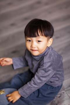 A cute Asian boy wearing a gray sweater plays indoors.