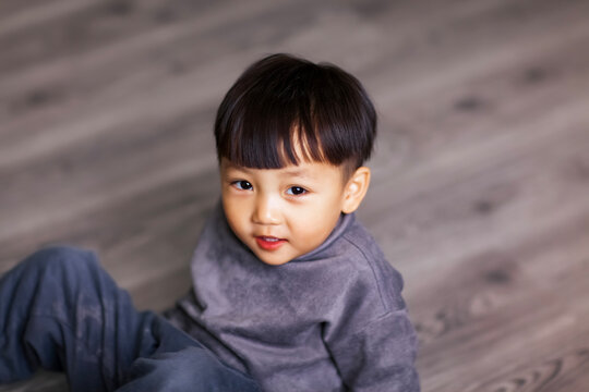 A cute Asian boy wearing a gray sweater plays indoors.
