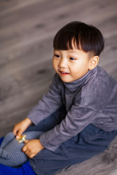 A cute Asian boy wearing a gray sweater plays indoors.