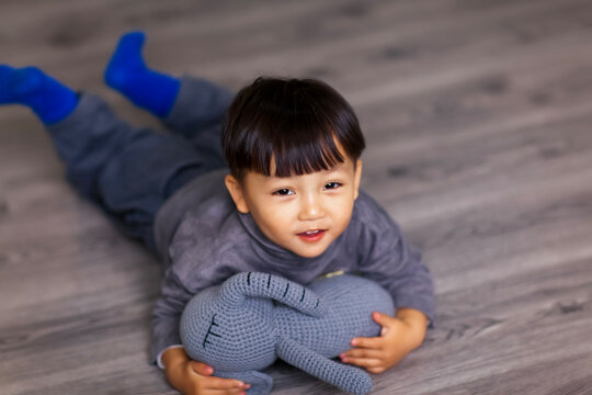 A cute Asian boy wearing a gray sweater plays indoors.