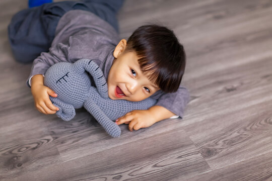A cute Asian boy wearing a gray sweater plays indoors.