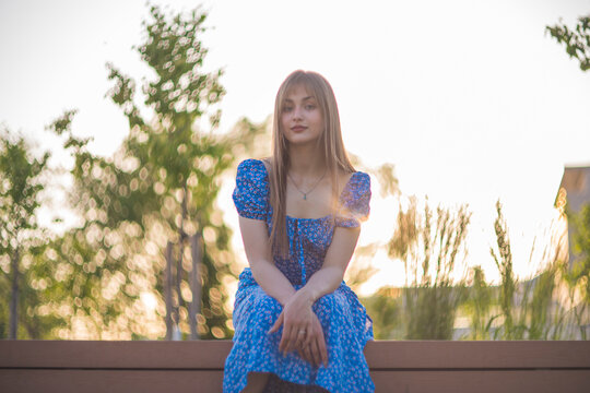 Gentle young woman in blue floral dress smiling in golden hour sunset with copy space