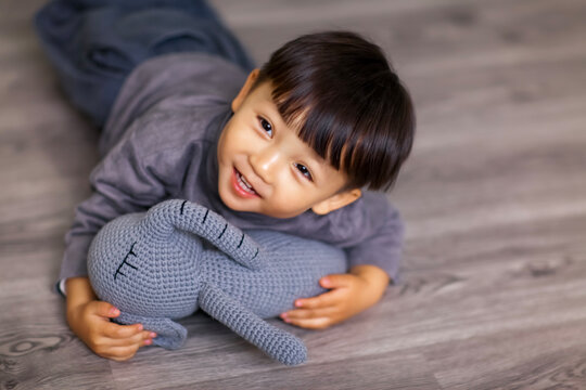 A cute Asian boy wearing a gray sweater plays indoors.