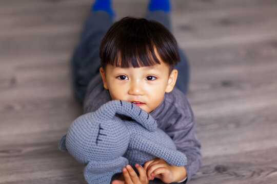 A cute Asian boy wearing a gray sweater plays indoors.