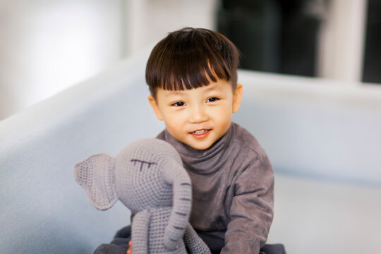 A cute Asian boy wearing a gray sweater plays indoors.