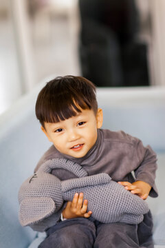 A cute Asian boy wearing a gray sweater plays indoors.