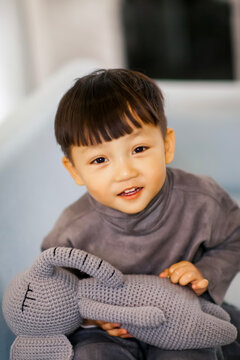 A cute Asian boy wearing a gray sweater plays indoors.