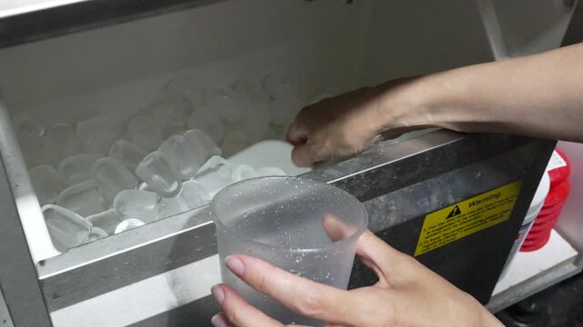 Ice scoop plastic cup filling frozen cubes at food service machine for beverage preparation in commercial kitchen environment